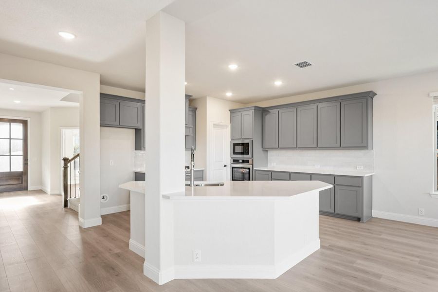 Open kitchen with gray cabinets, white island, stainless steel appliances, and light hardwood floors Open kitchen with gray cabinets, white island, stainless steel appliances, and light hardwood floors