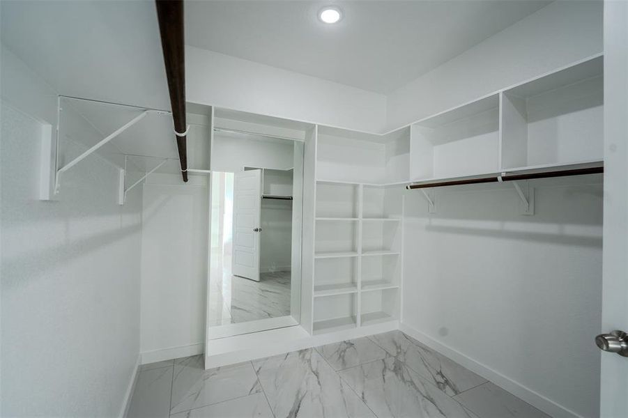 Spacious primary closet with light marble finish flooring Spacious primary closet with light marble finish flooring