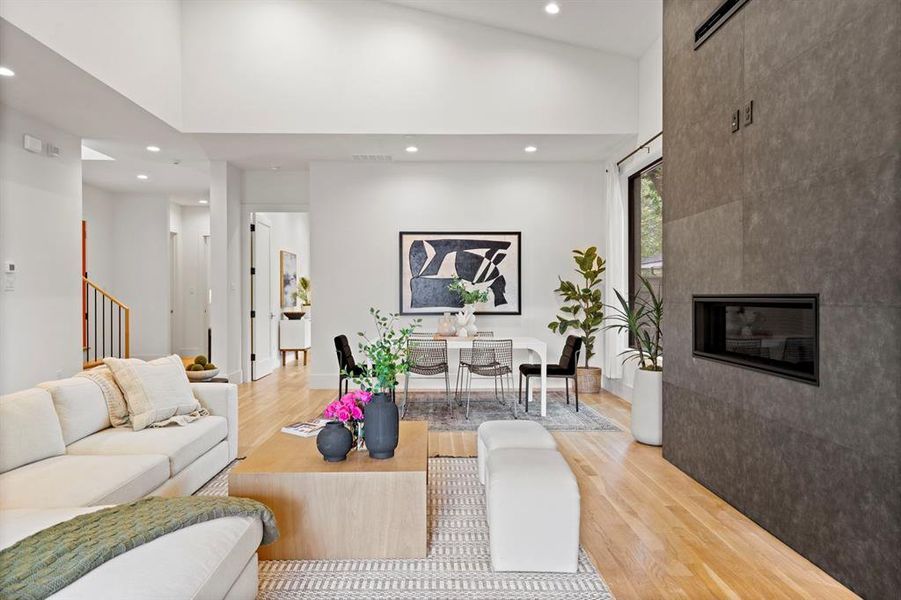 Living room with a high ceiling, light wood-style flooring, recessed lighting, stairs, and a tile fireplace Living room with a high ceiling, light wood-style flooring, recessed lighting, stairs, and a tile fireplace