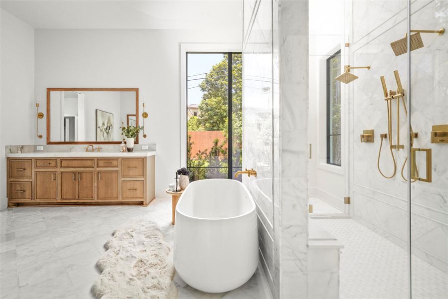 A closer look at the primary bath showcases marble tile, brass accents, warm wood cabinetry, and a bright, spa-inspired design.