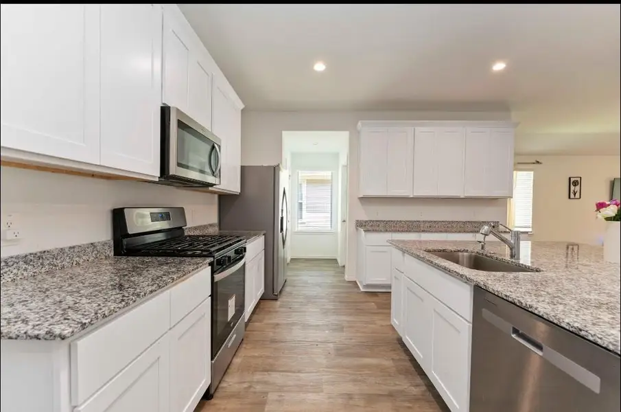 This kitchen features modern stainless steel appliances, granite countertops, and white cabinetry. The open layout includes a spacious island with a sink and dishwasher, complemented by wood-look flooring and recessed lighting. This kitchen features modern stainless steel appliances, granite countertops, and white cabinetry. The open layout includes a spacious island with a sink and dishwasher, complemented by wood-look flooring and recessed lighting.