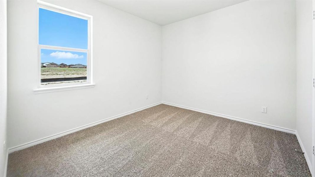 Bright interior space featuring a window with a white frame, light-toned walls, gray textured carpeting, and white baseboards