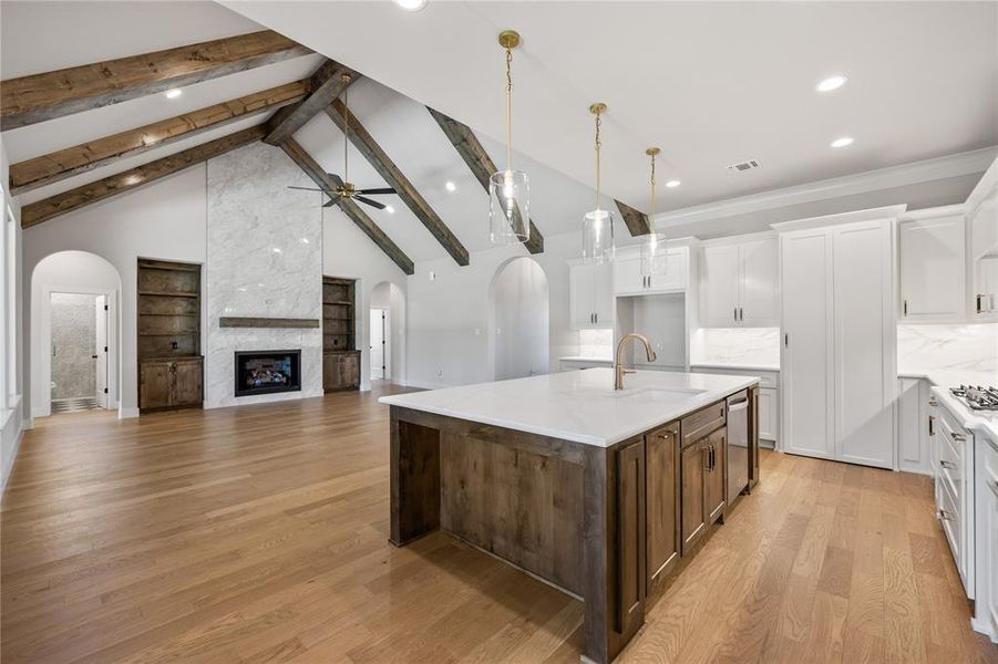 Dual tone kitchen with arched walkways, two tone cabinets, a kitchen island with sink, open floor plan, and built in shelves