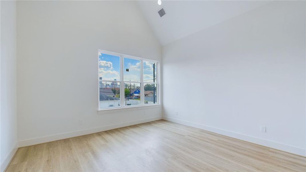 This thoughtfully designed primary bedroom features durable wood-like LVP flooring throughout. Cathedral ceilings are anchored by a stylish black ceiling fan, while oversized windows, paired with recessed lighting, illuminate the space. Enjoy breathtaking views of the downtown skyline right from your primary window.