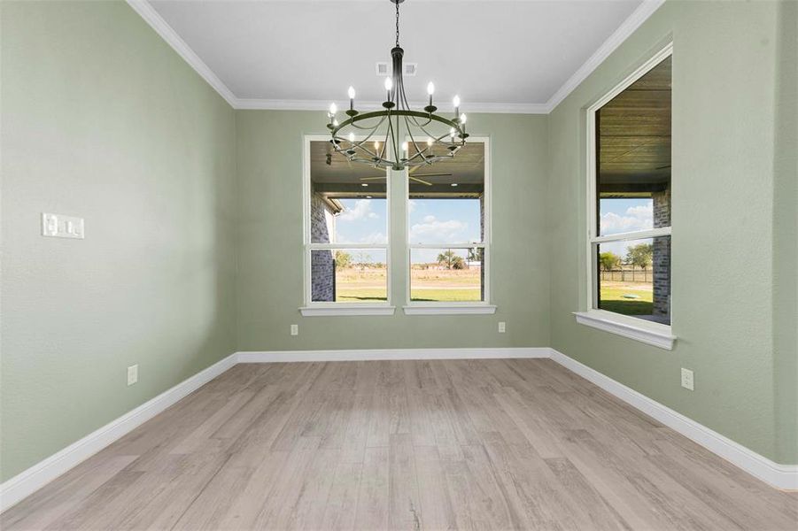 Breakfast room with light wood-type flooring, crown molding, and an inviting chandelier