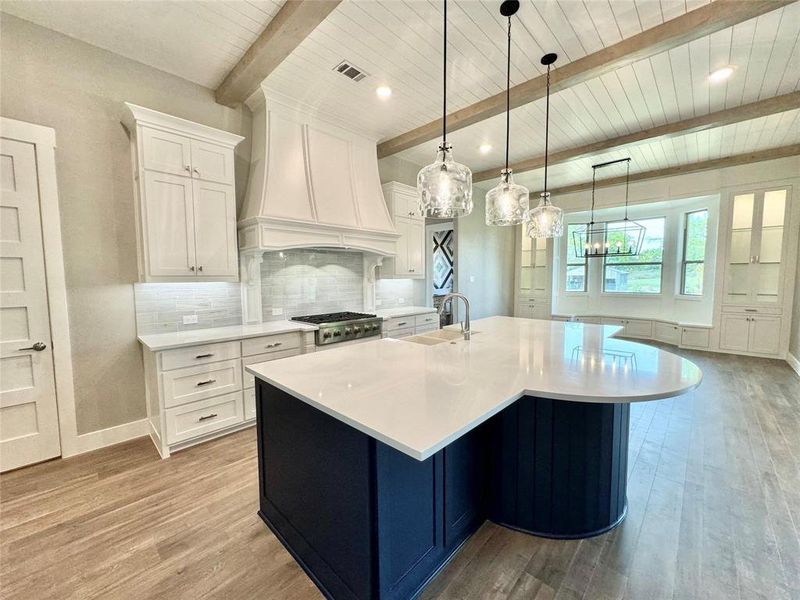 Kitchen with a sink, wood ceiling with exposed beams, light wood-style flooring, light countertops, and white cabinets
