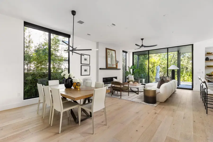 Dining space with light wood-style flooring, a wall of windows, a fireplace, a chandelier, and a ceiling fan Dining space with light wood-style flooring, a wall of windows, a fireplace, a chandelier, and a ceiling fan