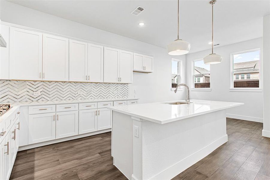 Kitchen with white cabinets, an island with sink, and hanging light fixtures