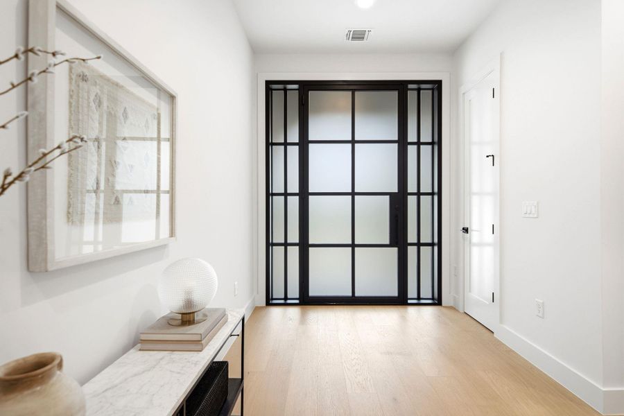Smooth wood floors and high ceilings frame a modern glass paneled entry door.