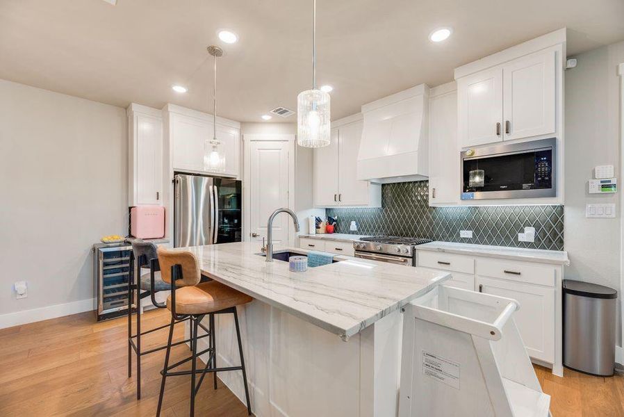 Kitchen featuring white cabinets, a kitchen bar, light stone countertops, a center island with sink, and stainless steel appliances