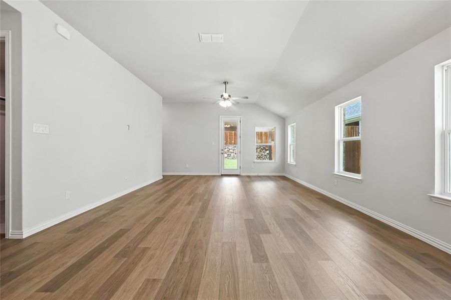 Unfurnished living room with ceiling fan, plenty of natural light, lofted ceiling, and wood finished floors Unfurnished living room with ceiling fan, plenty of natural light, lofted ceiling, and wood finished floors