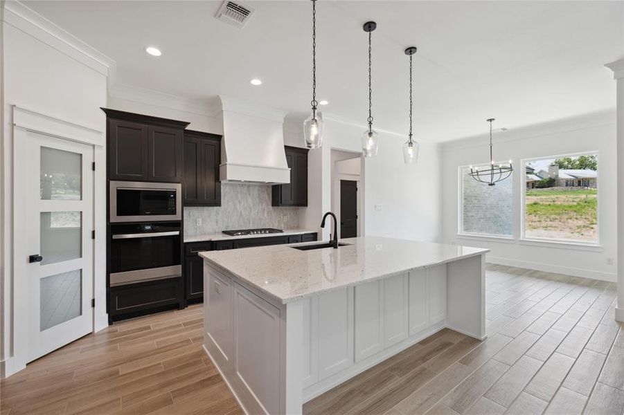 Kitchen with appliances with stainless steel finishes, custom exhaust hood, sink, decorative backsplash, and a center island with sink