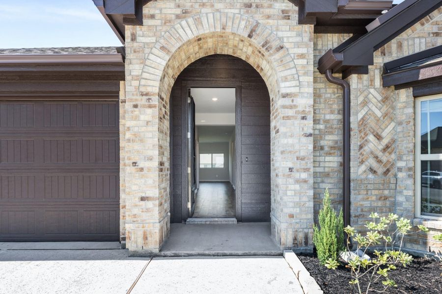 Home entrance with arched brick surround, dark front door, and attached garage with brown door.