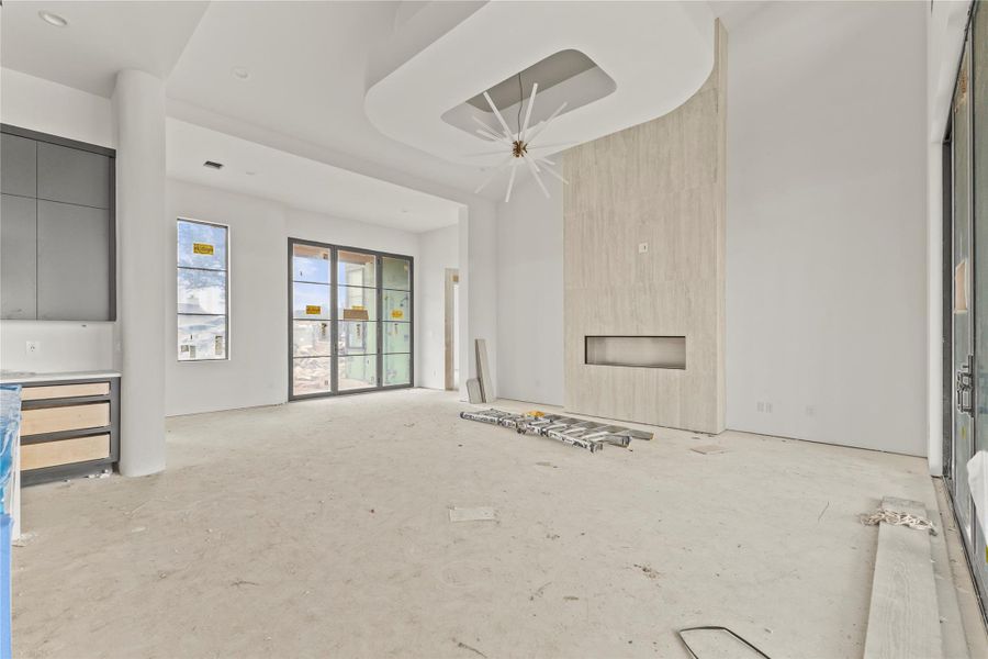 Spacious interior featuring a contemporary fireplace with a linear firebox, a distinctive ceiling light fixture, a curved architectural ceiling detail, and large multi-pane glass doors