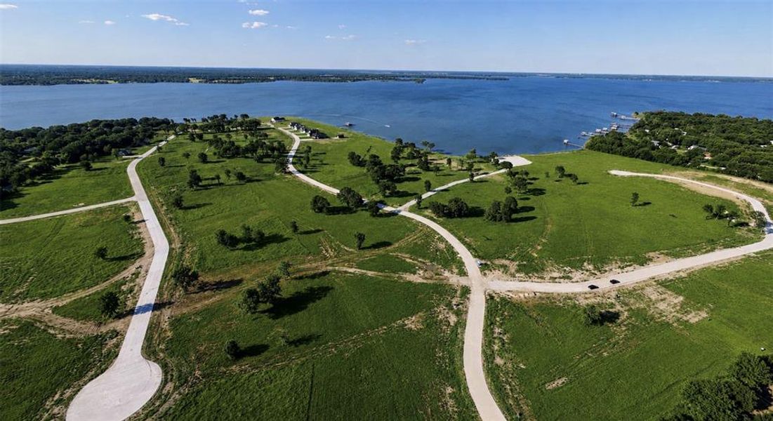 Expansive waterfront property featuring a large lake, verdant green fields, established trees, and paved roads Expansive waterfront property featuring a large lake, verdant green fields, established trees, and paved roads