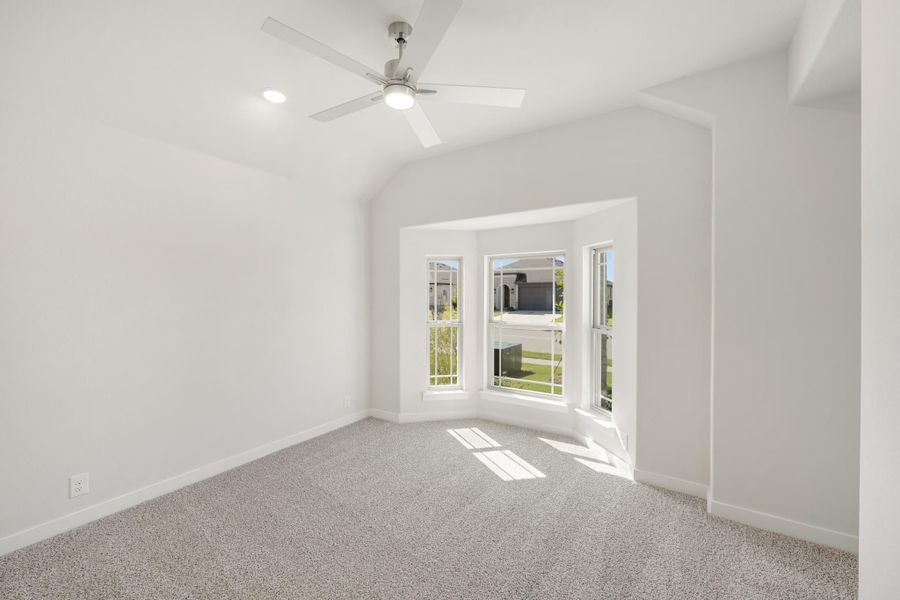 Empty bedroom with vaulted ceiling, ceiling fan, bay window, and gray carpet