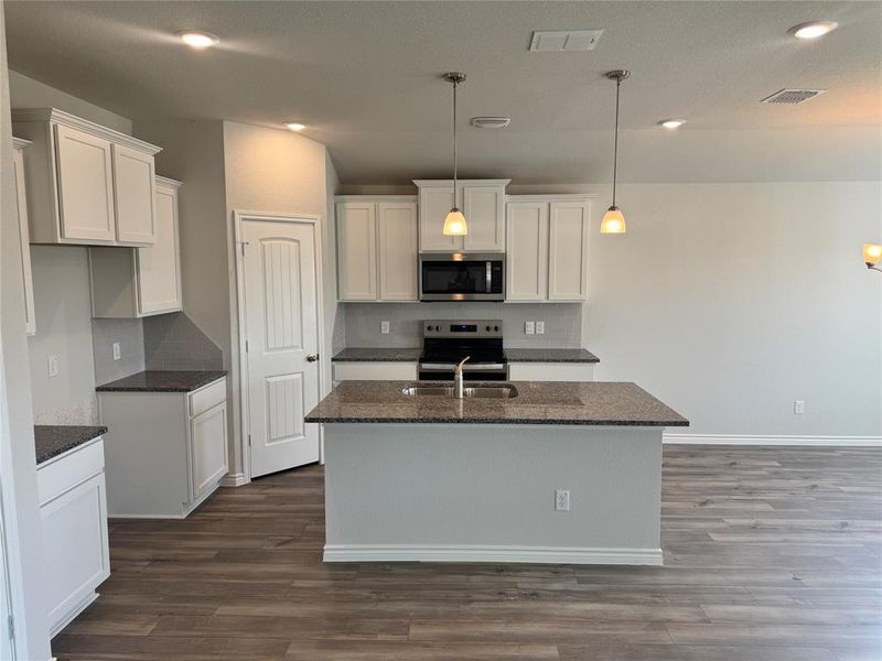 Kitchen featuring white cabinets, dark stone counters, stainless steel appliances, decorative light fixtures, and backsplash Kitchen featuring white cabinets, dark stone counters, stainless steel appliances, decorative light fixtures, and backsplash