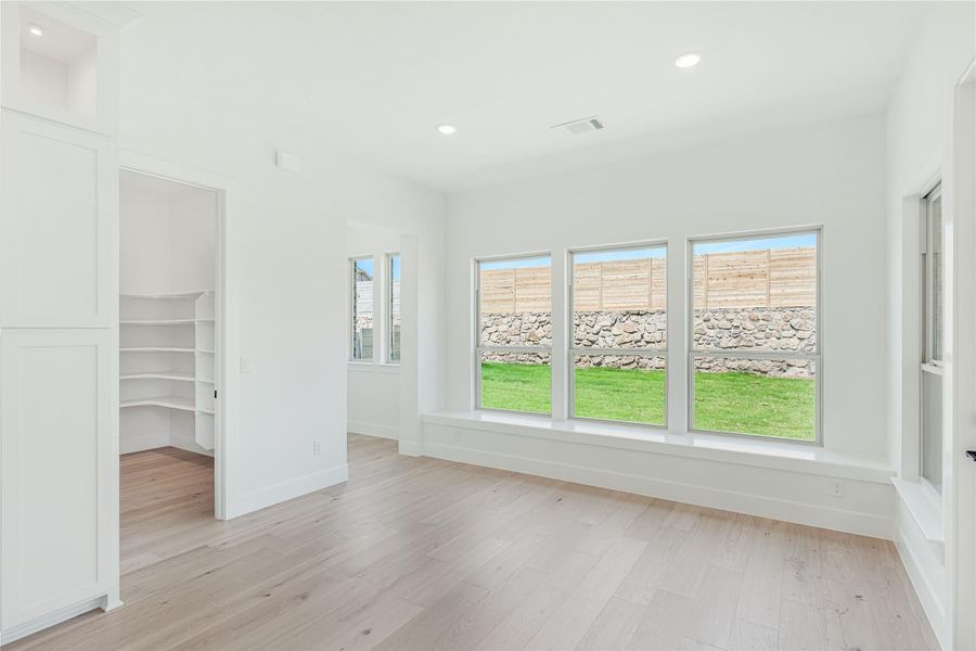 Empty bedroom with light hardwood floors, large windows, and walk-in closet entrance