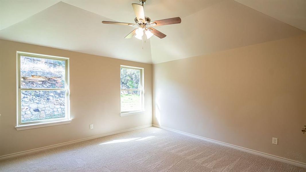 Carpeted empty room with lofted ceiling and a ceiling fan