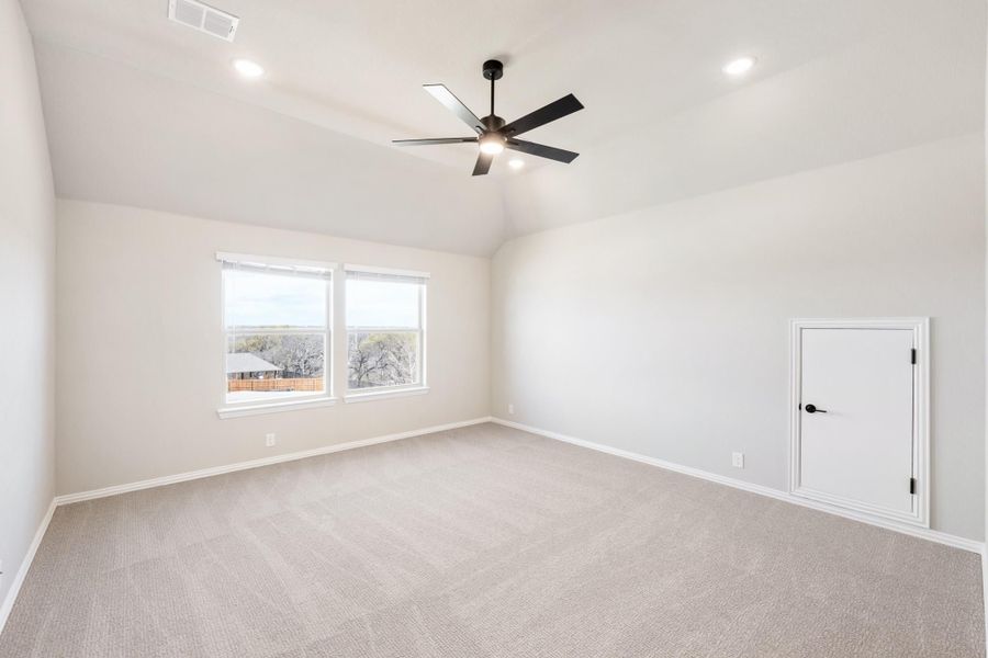 Empty bedroom with vaulted ceiling, ceiling fan, carpet flooring, and two windows with outdoor views
