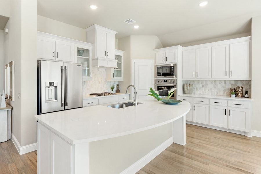 White kitchen with large curved island, stainless steel appliances, and light wood floors White kitchen with large curved island, stainless steel appliances, and light wood floors