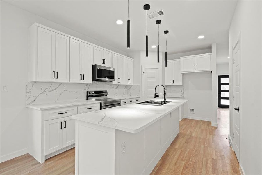 Kitchen with sink, hanging light fixtures, a center island with sink, appliances with stainless steel finishes, and white cabinets