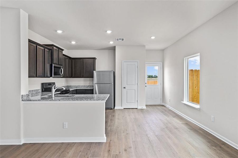 Kitchen with light stone countertops, stainless steel appliances, light wood-style flooring, recessed lighting, and a peninsula