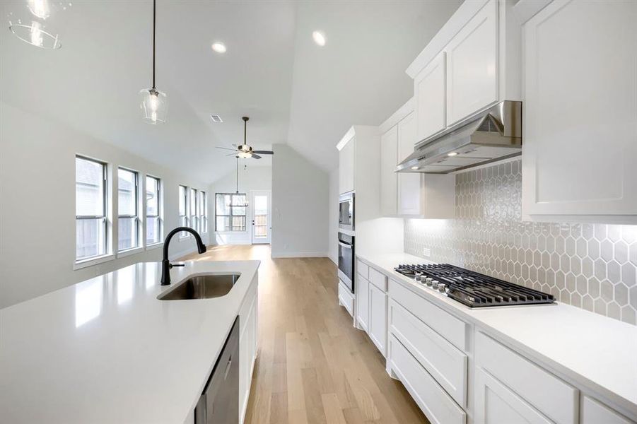 Spacious kitchen featuring white cabinetry, light-toned wood-finish flooring, a contemporary gas range, built-in microwave and oven, and a large island with an undermount sink Spacious kitchen featuring white cabinetry, light-toned wood-finish flooring, a contemporary gas range, built-in microwave and oven, and a large island with an undermount sink