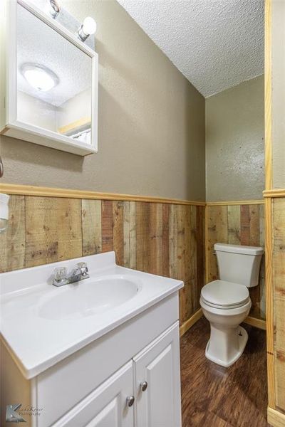 Half bathroom with a textured ceiling, wood finished floors, vanity, and a wainscoted wall