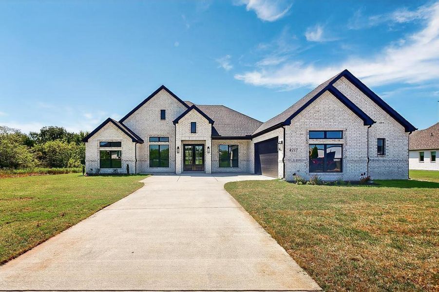 View of front of house with french doors, driveway, brick siding, an attached garage, and a front lawn