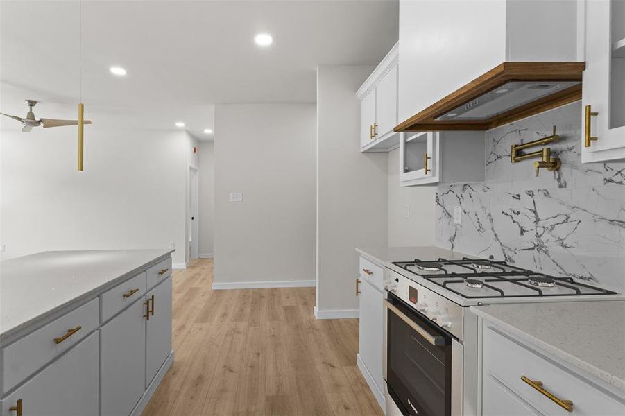 Kitchen featuring a gas range, white cabinetry with gold-finish hardware, a pot filler, and a stone-look backsplash