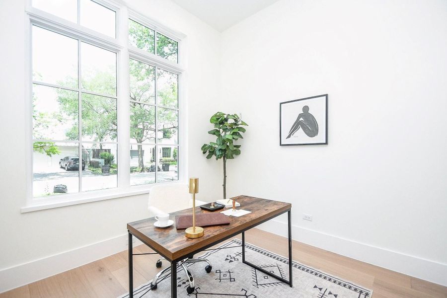 Bright home office with large windows, modern decor, and a minimalist wooden desk. The space features light walls, a framed artwork, and a potted plant, creating a serene and productive atmosphere.