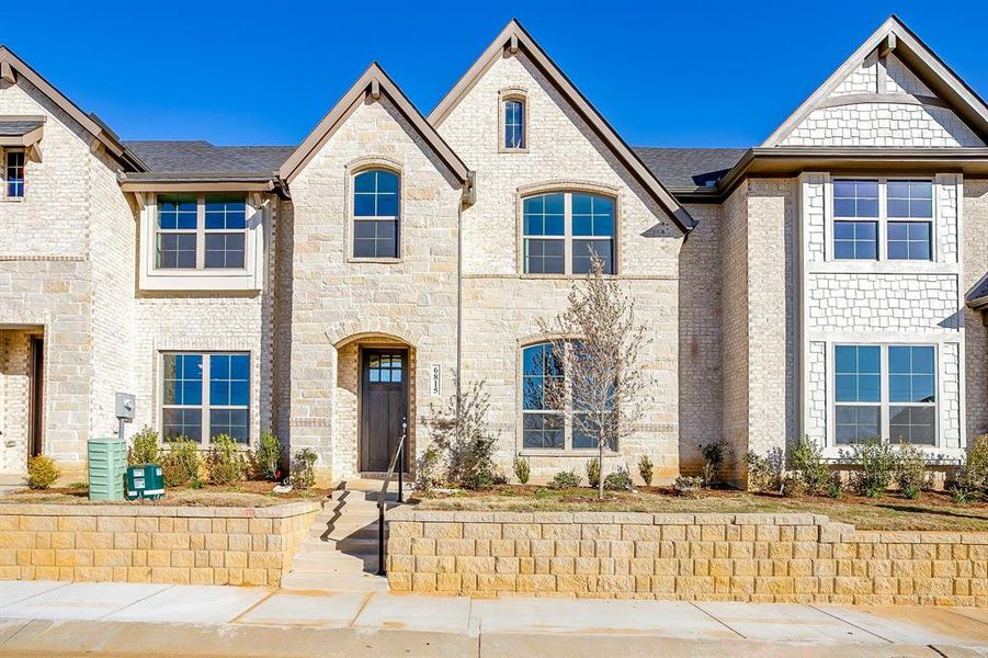 French country inspired facade featuring roof with shingles and stone siding