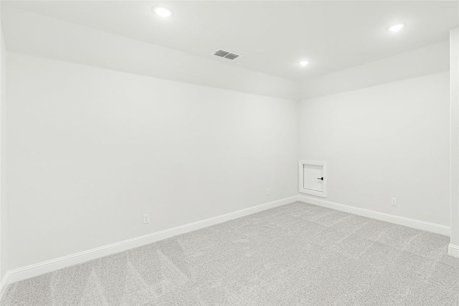 Empty room with white walls, gray carpet, recessed lighting, and a small wall access panel.