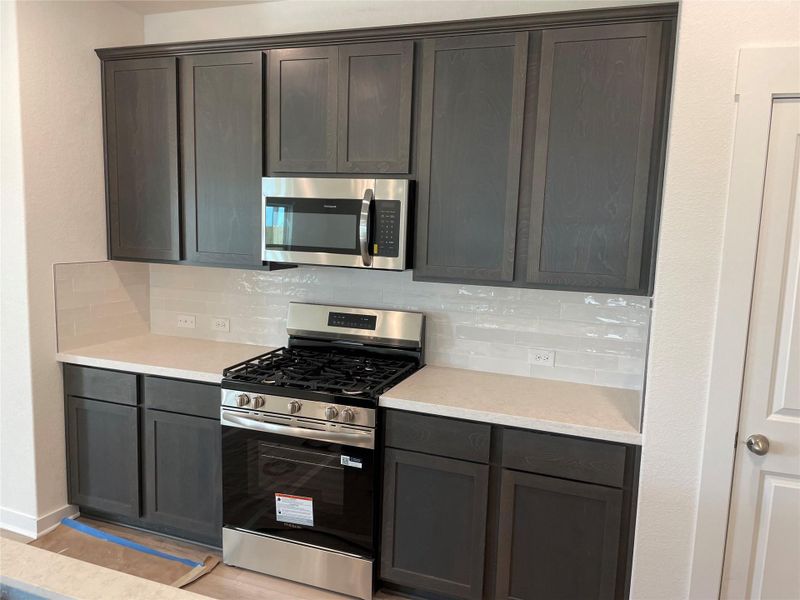 Kitchen with stainless steel appliances, tasteful backsplash, light stone counters, dark brown cabinets, and light wood finished floors Kitchen with stainless steel appliances, tasteful backsplash, light stone counters, dark brown cabinets, and light wood finished floors