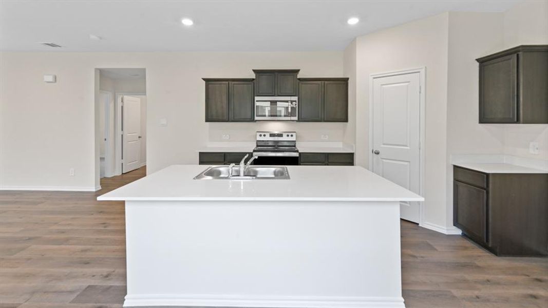 Kitchen featuring a large central island with an undermount sink, dark wood cabinetry, white countertops, and wood-finish flooring