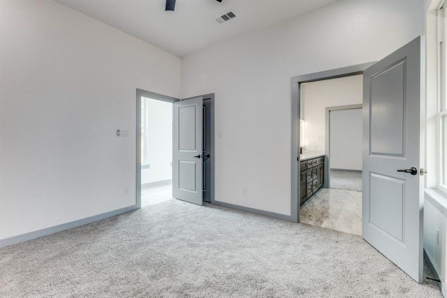 Unfurnished bedroom featuring ensuite bath, ceiling fan, and light carpet