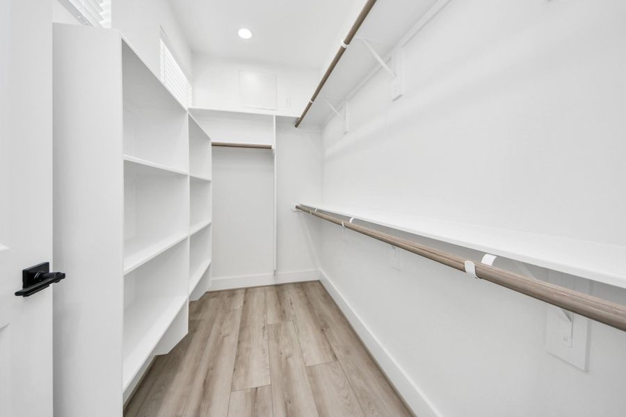 This photo shows a spacious walk-in closet with ample shelving and hanging space. It features light wood flooring, white walls, and recessed lighting, offering a bright and organized storage solution.