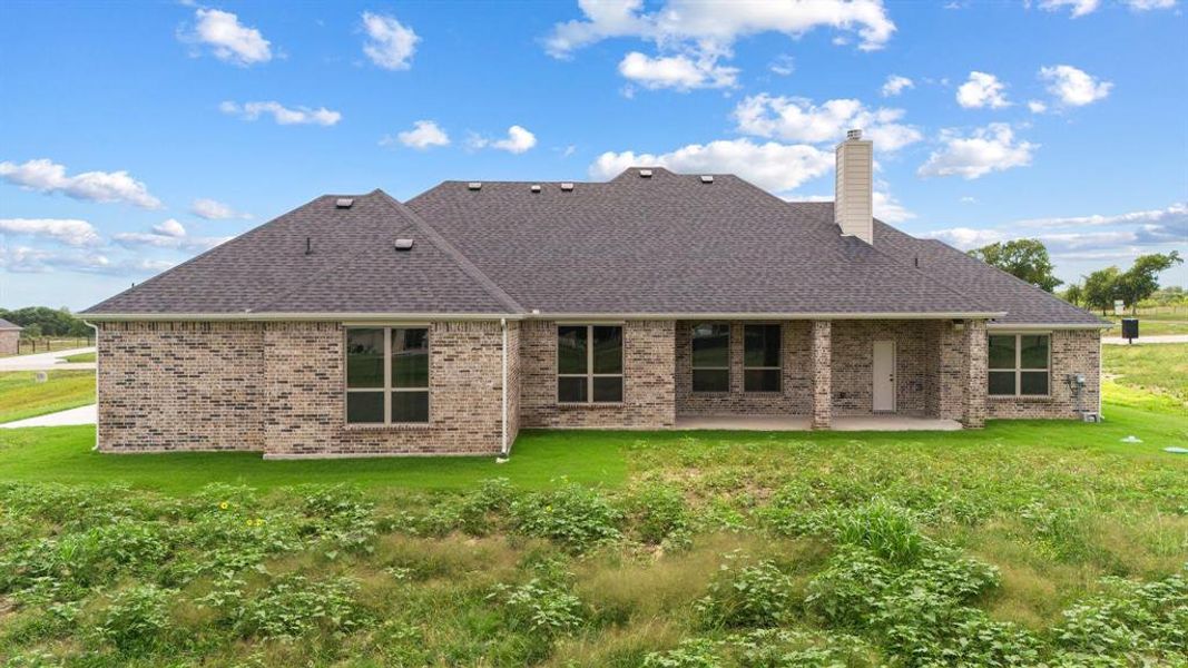 Back of house featuring a yard, a patio, brick siding, and a chimney