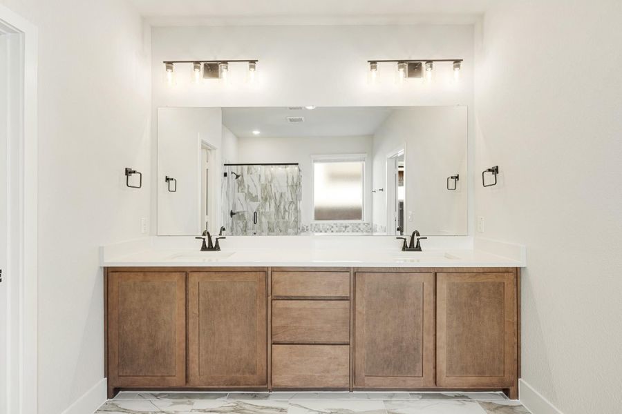 Bathroom double vanity with wood cabinets, white countertop, dual sinks, and large mirror with overhead lighting