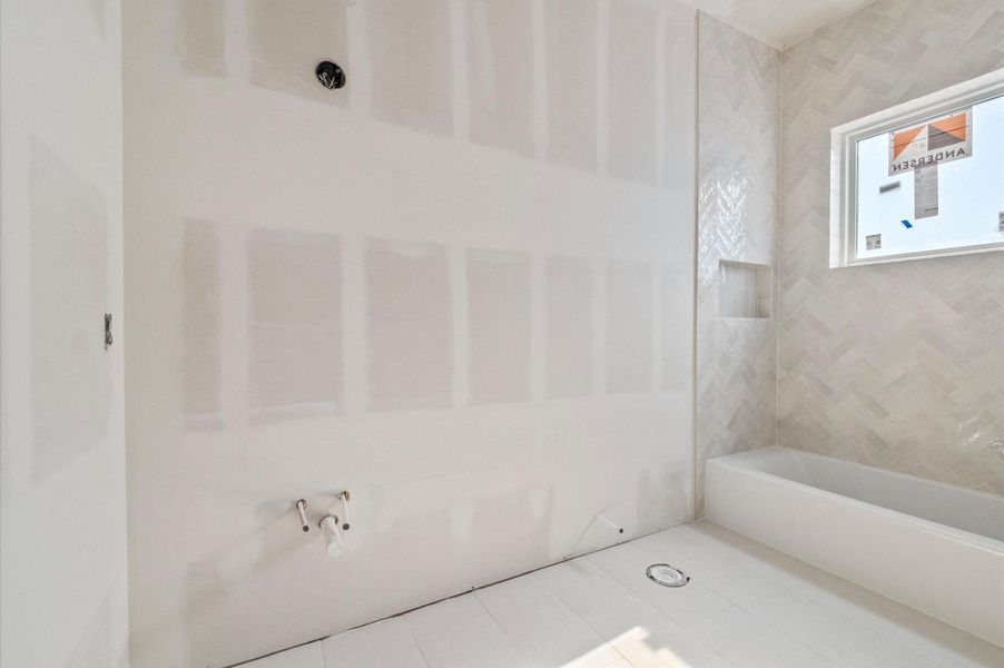 Third bathroom. This bathroom features a light herringbone shower with neutral tile flooring and a light gray cabinet to be installed. Polished chrome hardware will complete the space with a clean and cohesive finish.