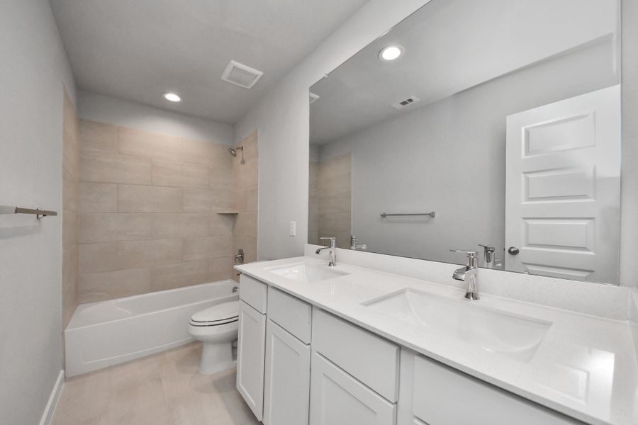 Secondary bath features tile flooring, bath/shower combo with tile surround, light stained wood cabinets, beautiful light countertop.