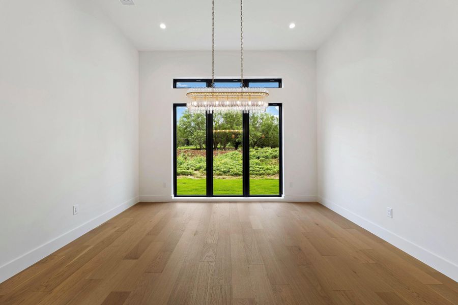 Expansive room featuring wood-finish flooring, a contemporary chandelier, recessed ceiling lighting, a large picture window, and a transom window above