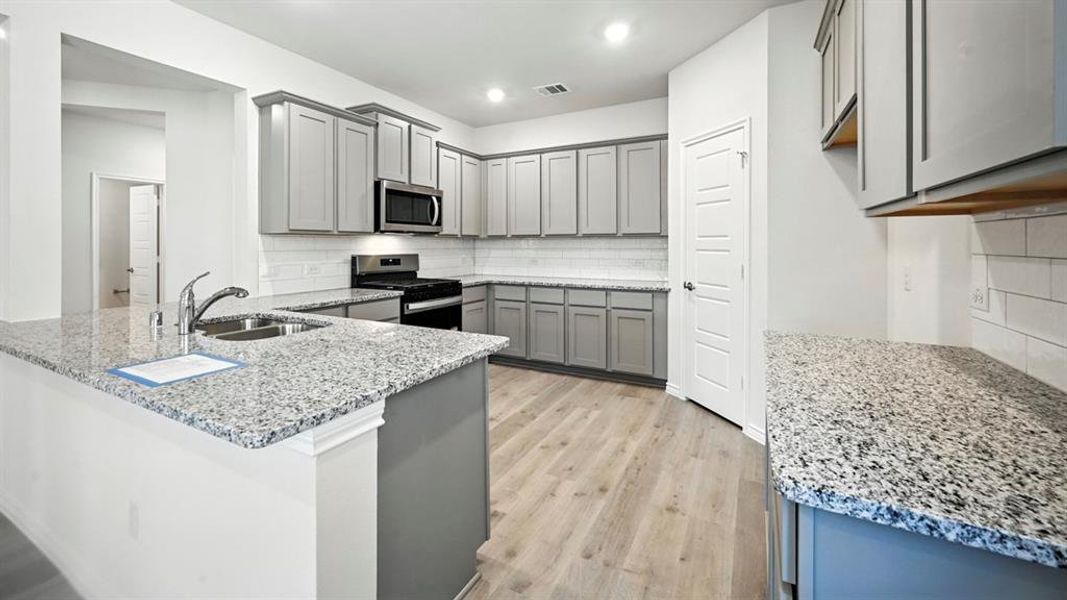 Kitchen with decorative backsplash, gray cabinets, light stone counters, stainless steel appliances, and light wood-style floors