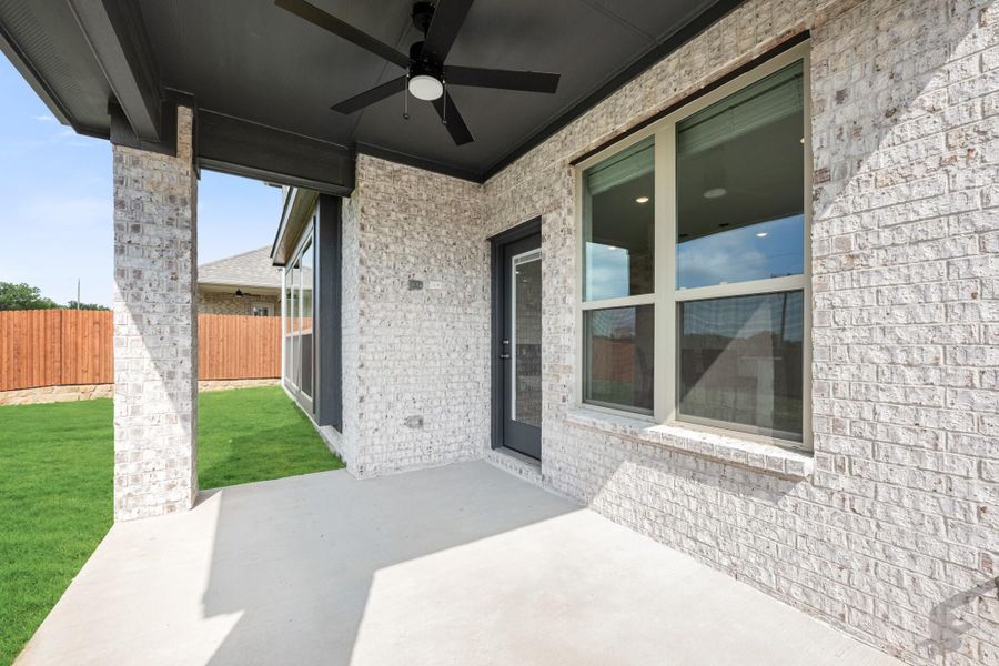 Covered back patio with ceiling fan, light brick exterior, concrete floor, and fenced backyard with green lawn