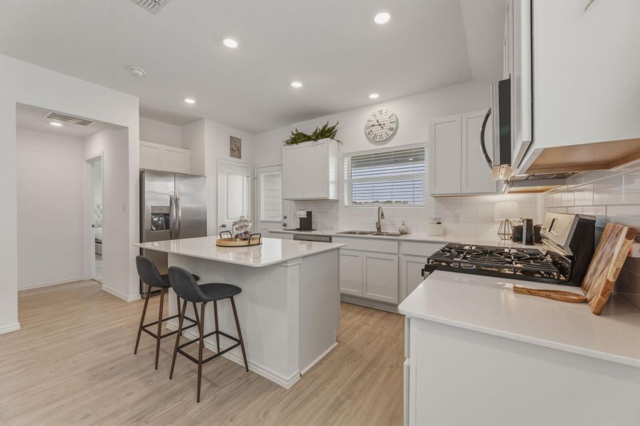 The kitchen features a central island with a countertop, stainless steel appliances, white cabinetry, and recessed lighting