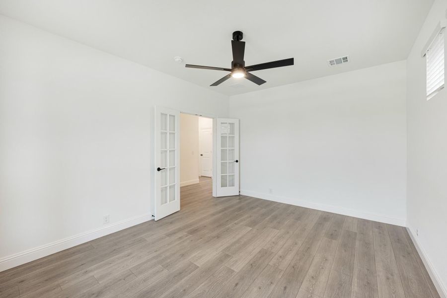 Empty room with hardwood floors, black ceiling fan, and white French doors leading to hallway Empty room with hardwood floors, black ceiling fan, and white French doors leading to hallway