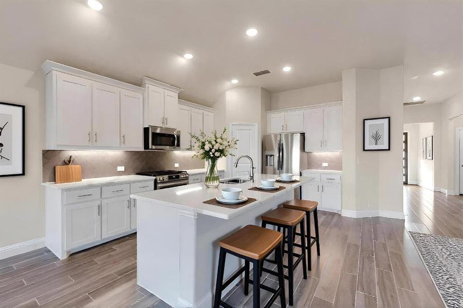 Kitchen featuring wood tiled floors, white cabinetry, an island with sink, a kitchen breakfast bar, and recessed lighting