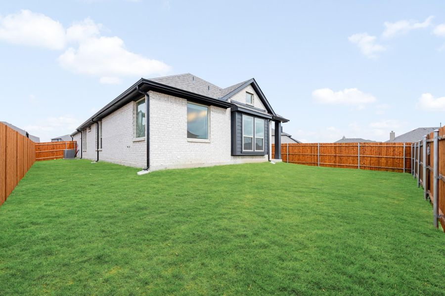 Backyard of single-story home with white brick exterior, green lawn, and wood privacy fence