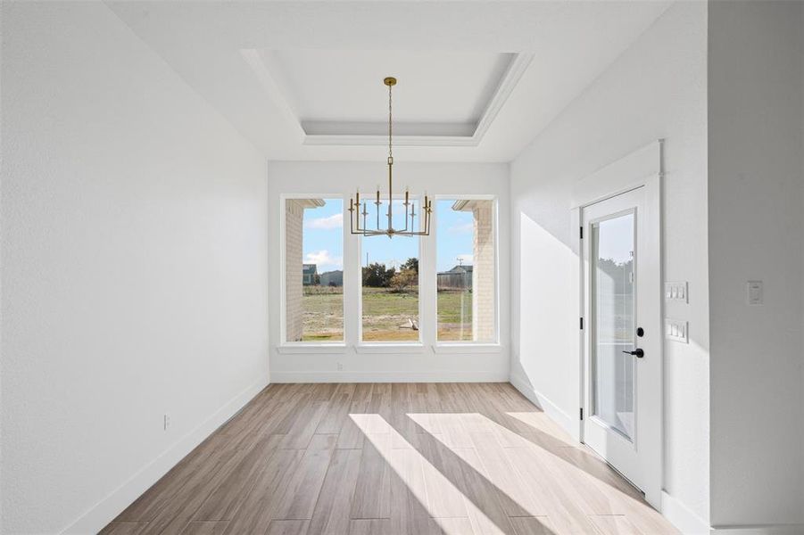 Unfurnished dining area featuring a chandelier, a raised ceiling, and light hardwood / wood-style flooring